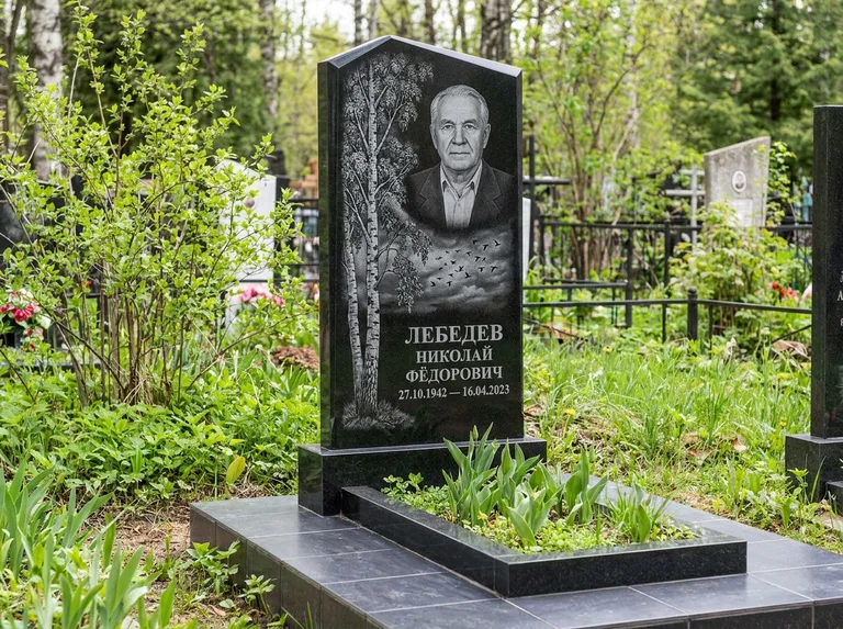 Памятник с гравировкой берёзы: вертикальная стела со скошенным верхом — берёза и стая птиц в небе, гранитный цоколь с тёмной плиткой, работа «Лебедев» в Якутске