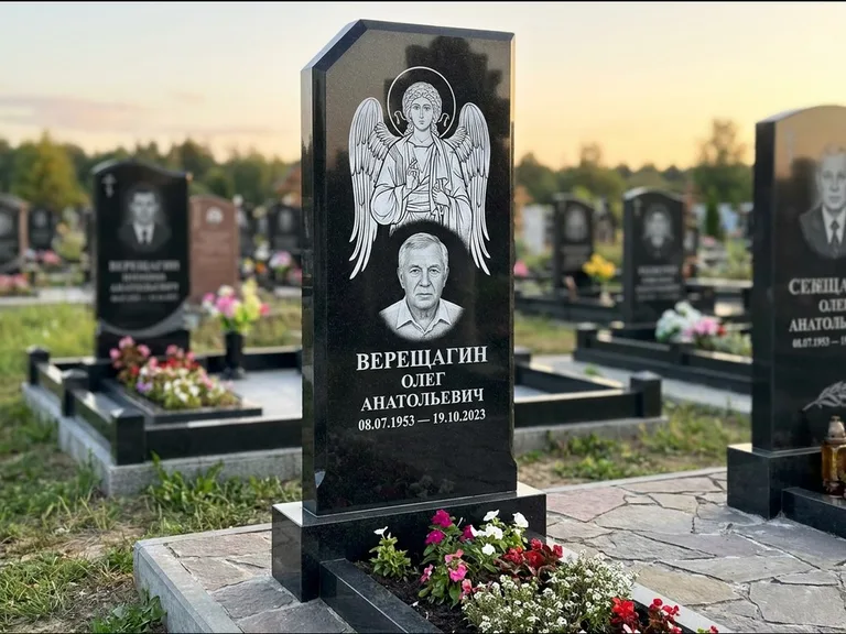 Памятник с гравировкой иконы: стела с резным навершием и нимбом в золоте — гравировка образа Спасителя, высокие разросшиеся туи полукругом, работа «Мельникова» в Якутске