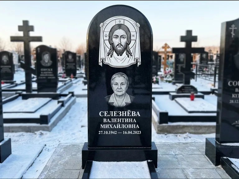 Памятник с гравировкой иконы: небольшая скромная одиночная стела с именной иконой — золочёный нимб на образе, аккуратный участок с газоном, работа «Ковалёв» в Якутске