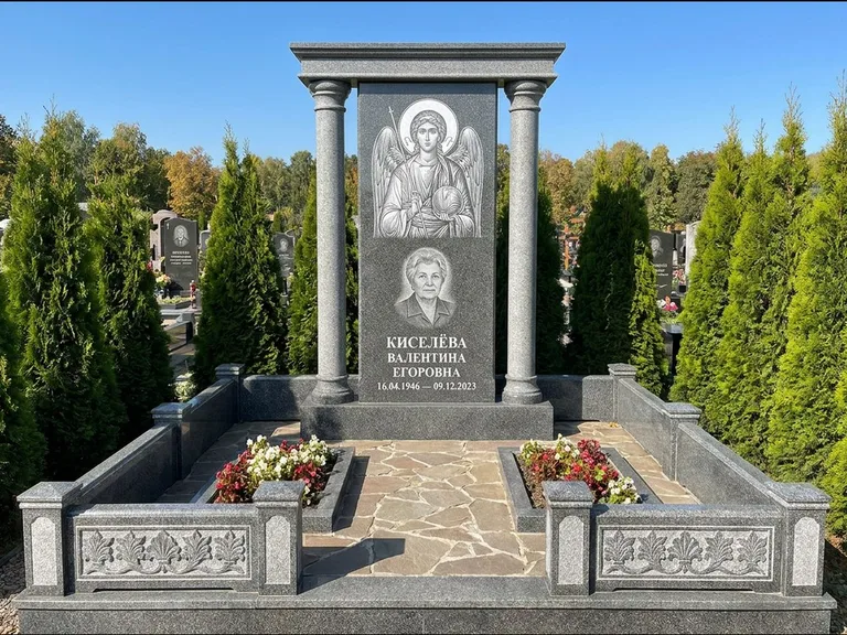 Памятник с гравировкой иконы: массивная стела с двускатным навершием-домиком — гравировка Николая Чудотворца, живая изгородь из туи, работа «Журавлёв» в Якутске