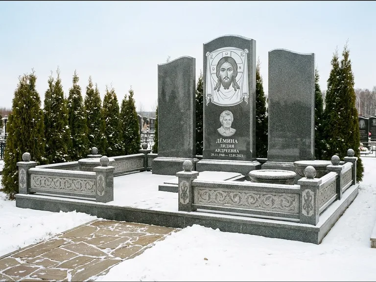 Памятник с гравировкой иконы: узкая вертикальная стела-пилон с ликом — икона в резной рамке-киоте, открытая лужайка без ограды, работа «Одинцов» в Якутске