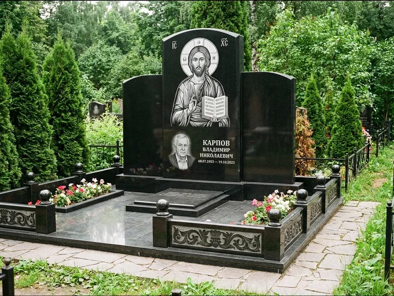 Памятник с гравировкой иконы: широкая панорамная стела с золочёным нимбом — гравировка образа Матроны Московской, цветник с белыми хризантемами, работа «Мельникова» в Якутске