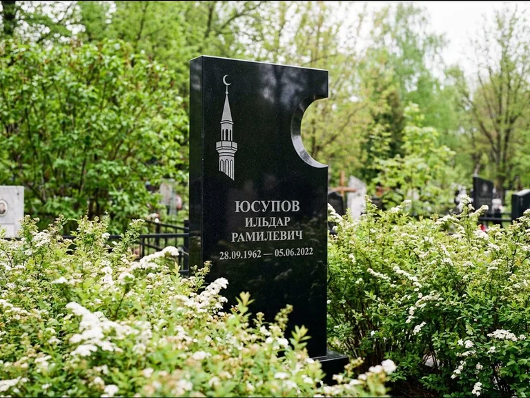 Мусульманский памятник с гравировкой мечети: стела с боковым вырезом в форме полумесяца — гравировка минарета с полумесяцем, низкие кусты спиреи в цвету, работа «Юсупов» в Якутске