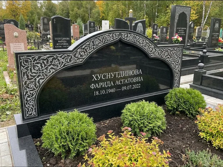 Мусульманский памятник: вытянутая горизонтальная семейная стела с аркой — белая гравировка силуэта мечети с минаретами, участок с декоративными кустами, работа «Зарипова» в Якутске